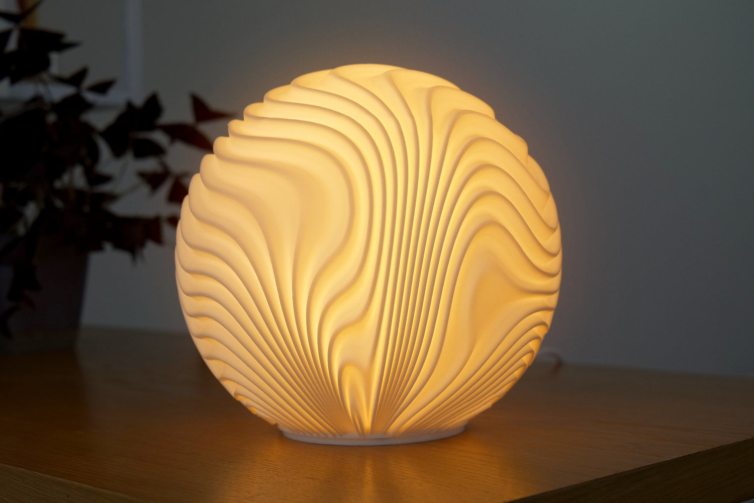 Round, textured lamp emitting a warm glow on a wooden surface with a blurred plant in the background.