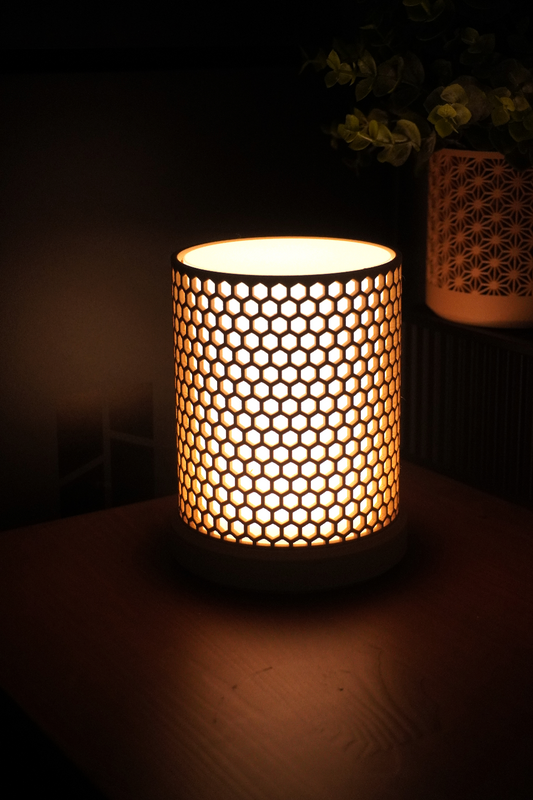 Cylindrical lamp with honeycomb pattern emitting warm ambient light on a wooden surface