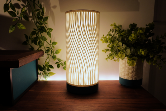 Tall cylindrical lamp with lattice pattern casting soft ambient light on a wooden surface