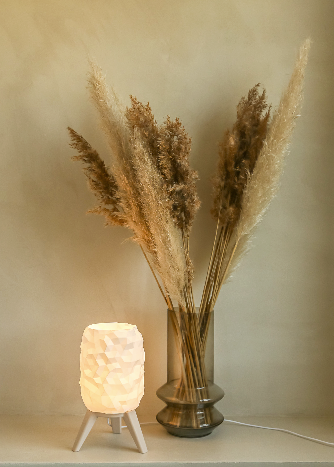 Lamp with textured white shade and dried pampas grass in a vase on a neutral background